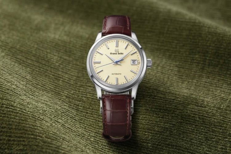 Orologio automatico Grand Seiko SBGR261 con quadrante avorio, lancetta dei secondi blu e cinturino in pelle marrone, adagiato su un elegante tessuto verde oliva.