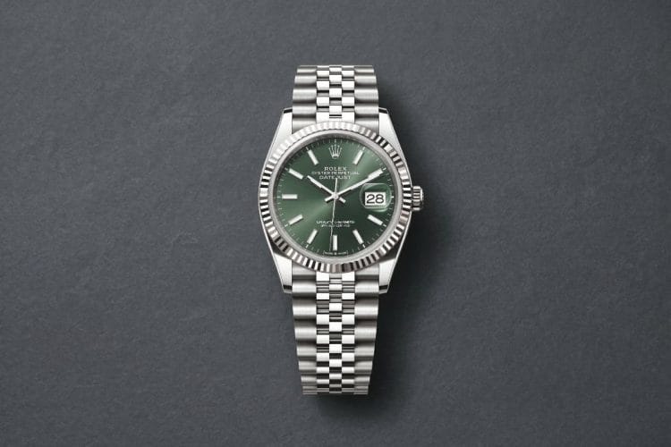 Rolex Datejust 36 con Quadrante Verde e Bracciale Jubilee Orologio Rolex Datejust 36 in acciaio con quadrante verde soleil, lunetta zigrinata e bracciale Jubilee, adagiato su un sobrio sfondo grigio scuro.