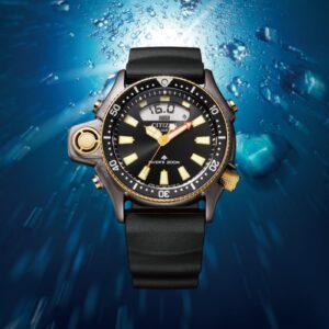 Citizen Aqualand JP2008-06E edizione limitata 40° anniversario, orologio subacqueo con cassa grigia spazzolata, dettagli oro rosa PVD, sensore di profondità a ore 9, display digitale e cinturino sostenibile BENEBiOL, fotografato in ambiente subacqueo con bolle d'aria.
