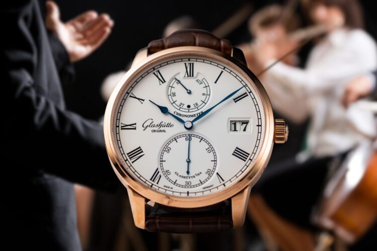 Glashütte Original Senator Chronometer con quadrante argentato e dettagli blu, che mostra le lancette delle ore e dei minuti al centro, i piccoli secondi alle 6, l'indicatore di riserva di carica alle 12 e il Panorama Date alle 3, cassa in oro rosso e cinturino in alligatore marrone.