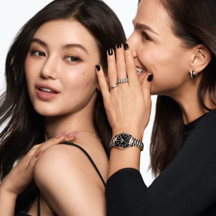 Scatto dalla campagna Omega "My Little Secret" con una modella che indossa l'orologio Seamaster Aqua Terra 30 mm e sussurra un segreto all'orecchio di un'altra.