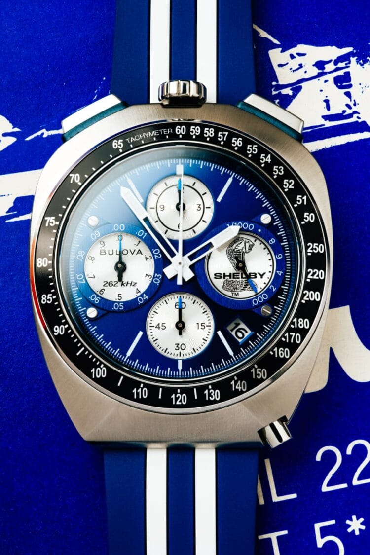 Bulova Shelby 150th Racer Chronograph (98B452) – macro del quadrante Primo piano Bulova Shelby Racer Chronograph 150th (98B452): quadrante blu soleil con contatori argento, logo cobra a ore 3, data a ore 4:30, cinturino blu a doppia striscia su sfondo blueprint