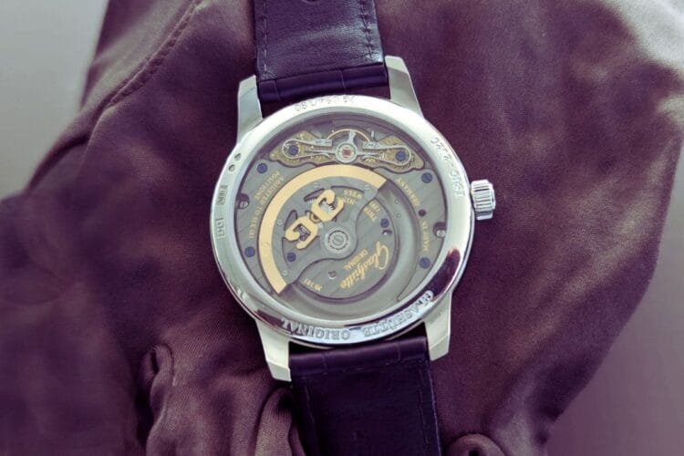 Calibro 92 in dettaglio: le decorazioni artigianali sassoni del movimento PanoMaticLunar Anniversary Edition fotografate dal vivo Fondello aperto del Glashütte Original PanoMaticLunar Anniversary Edition che rivela il calibro 92 con rotore dorato, coste di Glashütte, ponte del bilanciere decorato e finiture tradizionali sassoni del movimento di manifattura