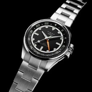 Timex Atelier GMT24 M1a con movimento Landeron 24, cassa acciaio 40mm, quadrante smaltato nero e lancetta GMT arancione su bracciale acciaio.