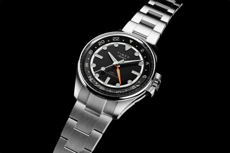 Timex Atelier GMT24 M1a con movimento Landeron 24, cassa acciaio 40mm, quadrante smaltato nero e lancetta GMT arancione su bracciale acciaio.