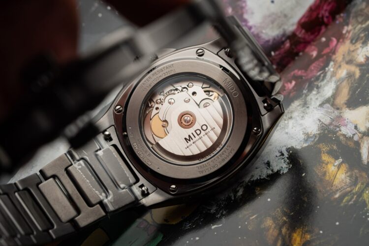 Il Calibro 80 visto dal fondello trasparente Il fondello trasparente del Mido Multifort TV S01E02, che rivela il movimento automatico Calibro 80 e la massa oscillante decorata con Côtes de Genève.