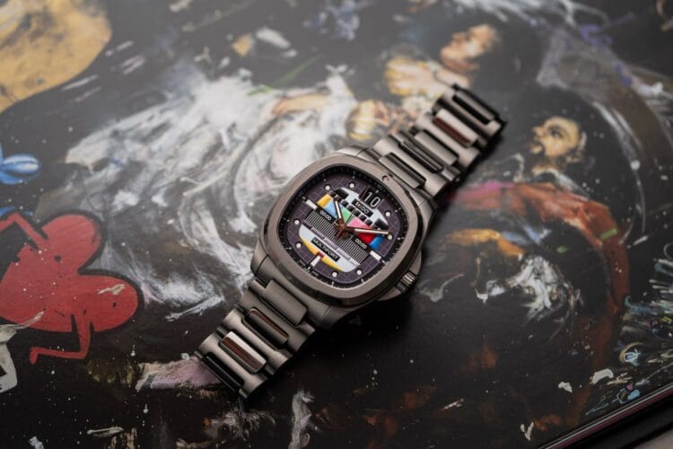 La finitura PVD grigio industriale del Mido S01E02 Il Mido Multifort TV S01E02 posato su una superficie artistica, che mostra l'intera cassa a cuscino e il bracciale integrato con la finitura PVD grigio satinato.