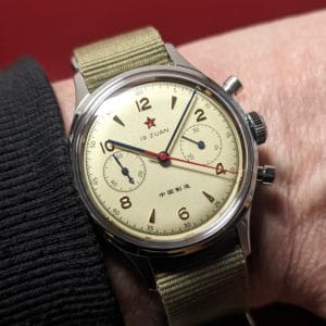 Foto live orologio cronografo meccanico Seagull 1963 con quadrante 19 Zuan color crema, stella rossa e cinturino NATO verde, in primo piano su sfondo sfocato.