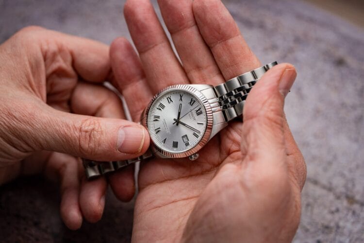 Tissot Ballade COSC 39mm - Dimensioni reali e vestibilità del cronometro certificato Tissot Ballade COSC da 39mm tenuto in mano che mostra dimensioni reali della cassa in acciaio, lunetta zigrinata, quadrante a raggi e bracciale a cinque maglie lucido spazzolato.