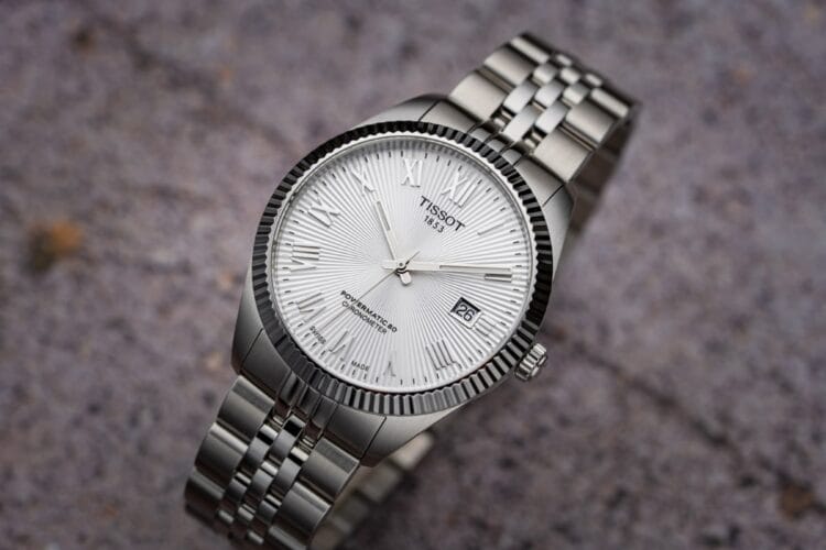 Tissot Ballade COSC Powermatic 80 Chronometer con quadrante argentato motivo a raggi, lunetta zigrinata, numeri romani applicati, bracciale acciaio cinque maglie.