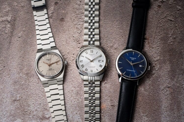 Tissot Powermatic 80 - Confronto PRX Titanium, Ballade COSC e Classic Dream Confronto flat lay Tissot Powermatic 80: PRX Titanium con quadrante petite tapisserie e bracciale integrato, Ballade COSC con lunetta zigrinata e numeri romani, Classic Dream con quadrante blu e cinturino pelle.
