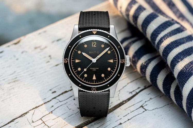 Baltic Aquascaphe Classic Black Gilt con quadrante nero e indici dorati gilt, cinturino nero in pelle, su tavola di legno bianco scrostato con tessuto a righe marinare.