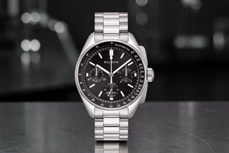 Bulova Lunar Pilot 43,5 mm con quadrante nero, tre contatori cronografici e bracciale in acciaio, su superficie metallica con sfondo bokeh scuro.