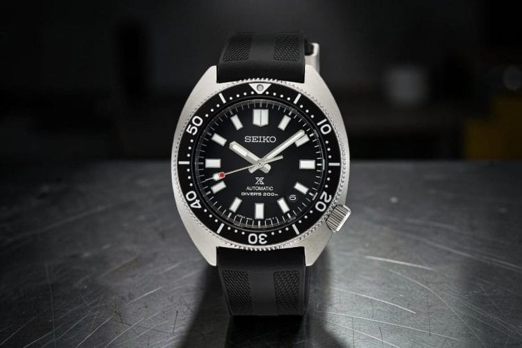 Seiko Prospex SPB317J1 con cassa a forma di tartaruga, quadrante nero, lunetta nera e cinturino in gomma, su superficie in acciaio spazzolato.