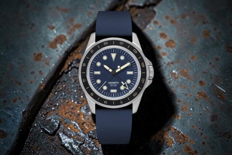 Unimatic U1-GMT-DHN con quadrante blu navy, ghiera 24h nera e cinturino in gomma, poggiato su superficie metallica ossidata e corrosa.