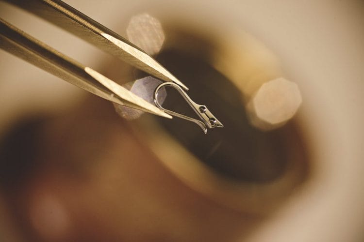 Black polishing Glashütte Original: la molla a collo di cigno e il paradosso ottico della lucidatura nera Molla a collo di cigno Glashütte Original tenuta da pinzette: la superficie lucidata con la tecnica del black polishing.