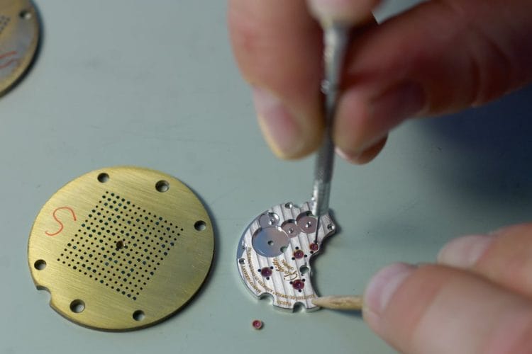 Inserimento castoni in oro Glashütte Original: precisione alla scala del decimo di millimetro Orologiaio Glashütte Original inserisce un castone in oro su un ponte del calibro con pinzette di precisione.