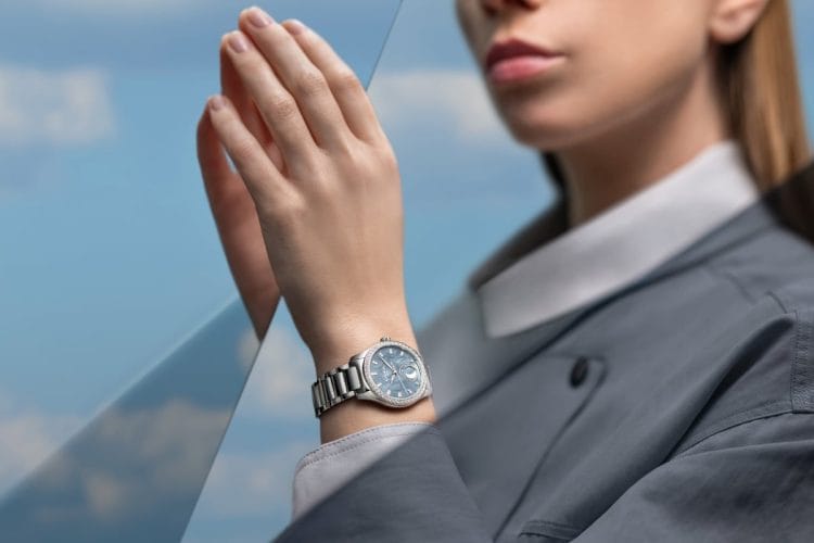 Donna con Glashütte Original Serenade Luna Skyline Blue al polso davanti a un cielo urbano.