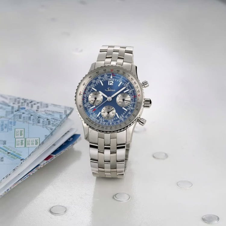 Sinn 903 Ti II Anniversary con quadrante blu, regolo calcolatore e bracciale in titanio Grado 5 accanto a una mappa.