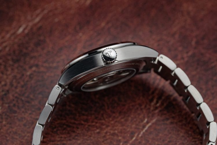 Tissot Gentleman 38 mm: Dettaglio del profilo e del vetro zaffiro Vista laterale della cassa in acciaio 316L del Tissot Gentleman 38 mm, con focus sulla corona logata, le finiture satinate e la curvatura elegante del vetro zaffiro bombato.
