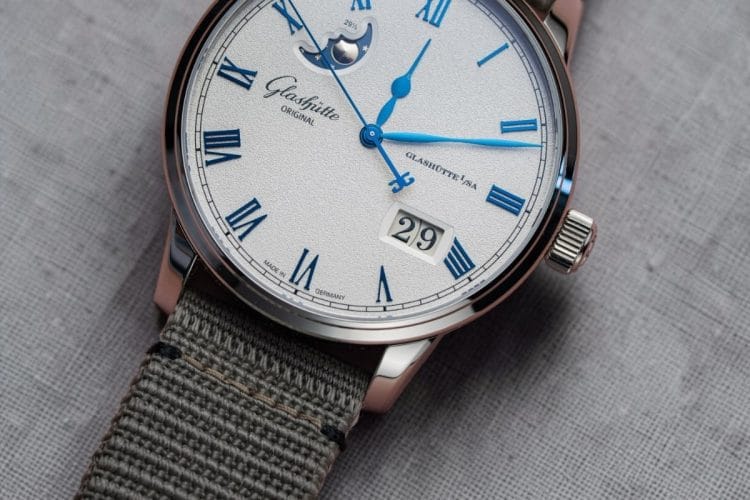 Glashütte Original Senator Excellence Panorama Date Moon Phase con cinturino in tessuto sintetico appoggiato su panno di lino grigio.