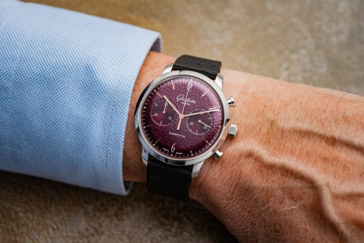 Glashütte Original Sixties Chronograph Annual Edition 2026 — al polso Glashütte Original Sixties Chronograph Annual Edition 2026 al polso: il cronografo da 42 mm con quadrante viola e cinturino in tessuto sintetico nero indossato con una camicia azzurra.