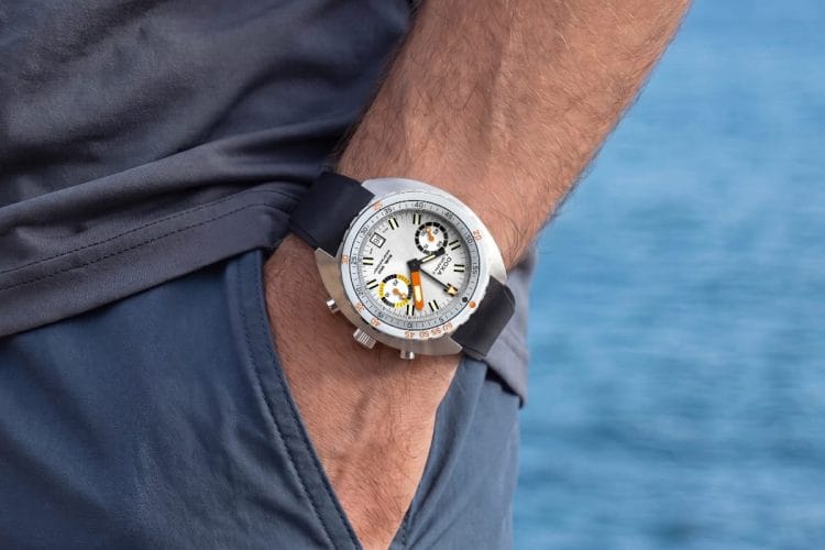 Doxa SUB 200 T.Graph II Searambler - La vestibilità al polso Doxa SUB 200 T.Graph II Searambler argento indossato al polso con sfondo mare, cinturino in caucciù nero.