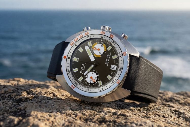 Doxa SUB 200 T.Graph II Sharkhunter - Cinturino in caucciù Doxa SUB 200 T.Graph II Sharkhunter con quadrante nero e cinturino in caucciù appoggiato su roccia, sfondo mare.
