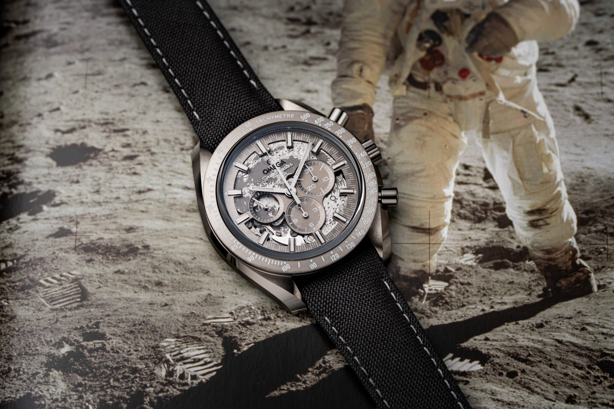 Omega Speedmaster Grey Side of the Moon in ceramica al plasma grigia su cinturino nylon, posato su stampa fotografica lunare con astronauta NASA sullo sfondo.