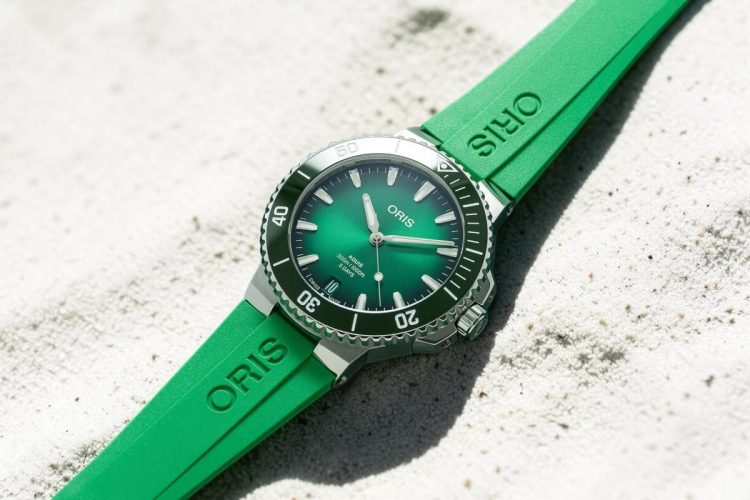 Oris Aquis Date Calibre 400 - orologio da mare estate 2026 Oris Aquis Date Calibre 400 con cinturino verde su sabbia chiara, orologio da mare estate 2026.